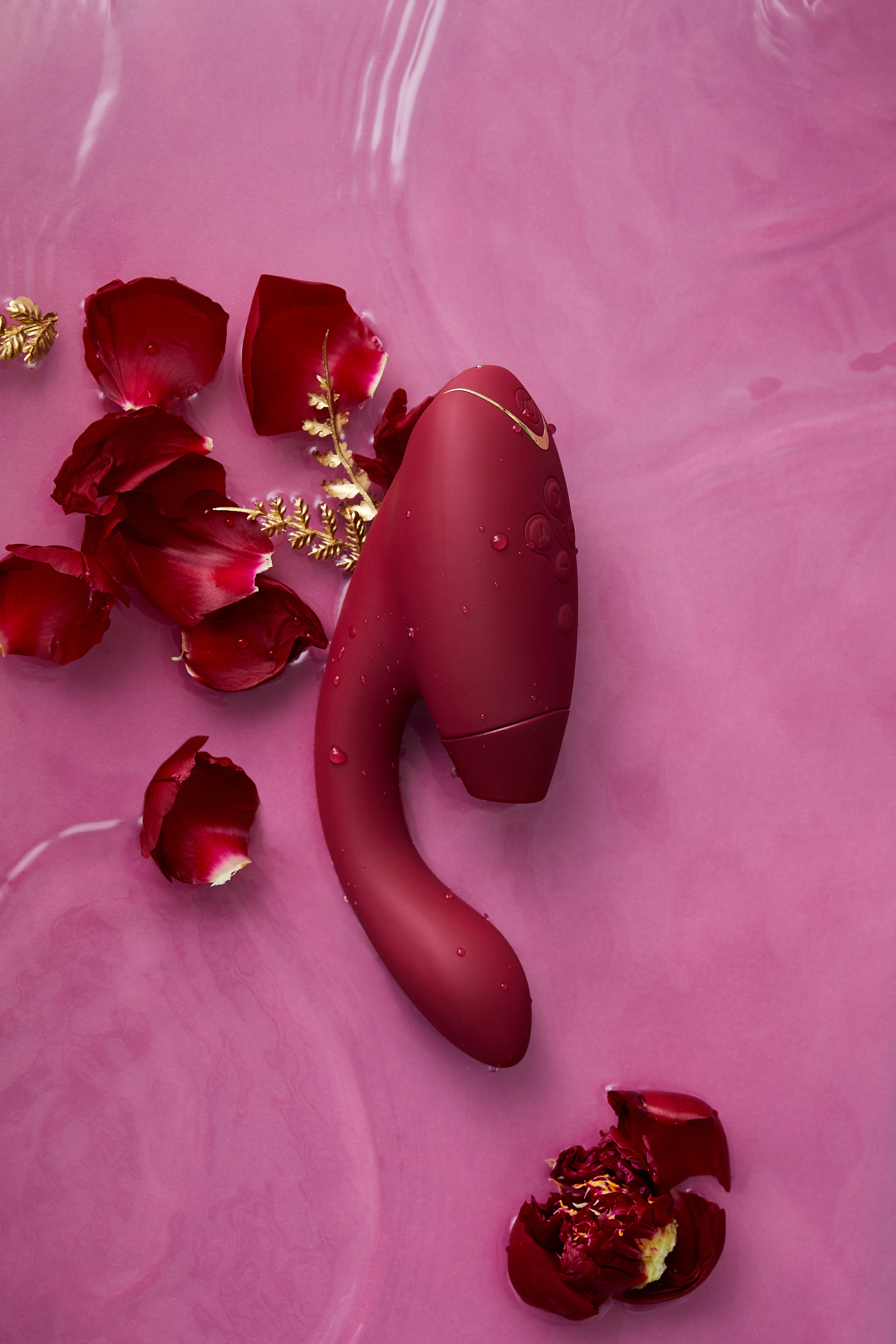 Womanizer Duo 2 in Burgundy against a pink background surrounded by flowers.